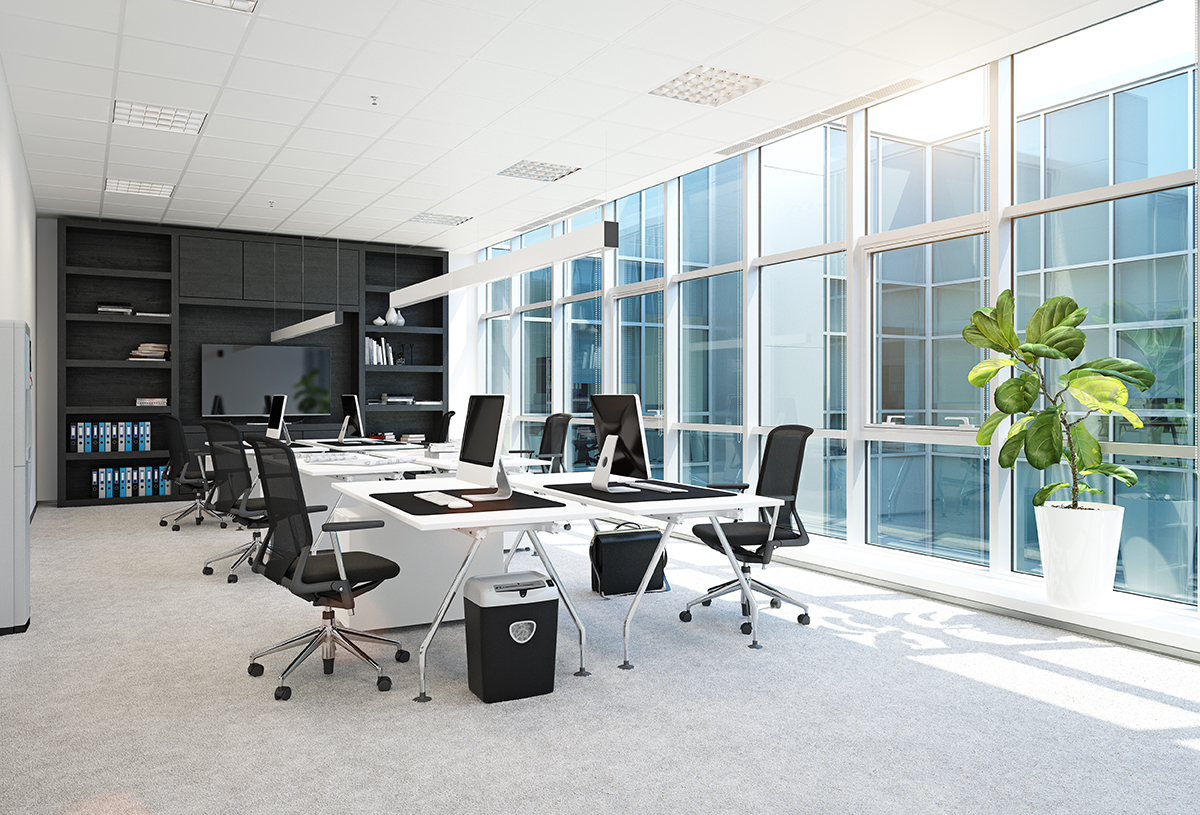 A bright, modern office space featuring ergonomic chairs, sleek white desks with desktop computers, built-in shelving, and large floor-to-ceiling windows allowing natural light to fill the room.