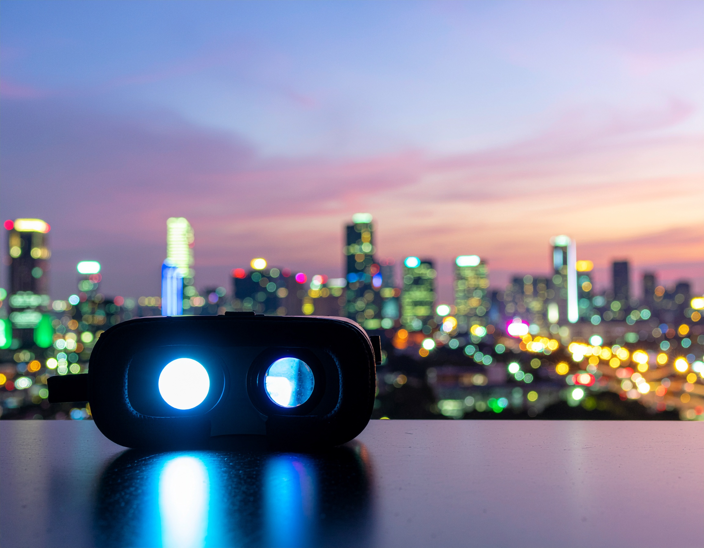 Virtual reality headset glowing on a tabletop with a vibrant, blurred city skyline in the background at sunset, symbolizing futuristic tech in urban settings